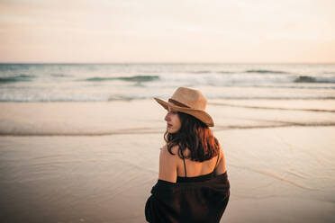 Young woman in hat looking away while standing at beach - GRCF00860