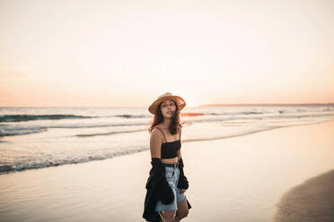 Junge Frau steht am Strand bei Sonnenuntergang - GRCF00865