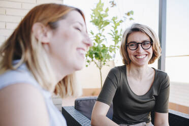 Smiling businesswoman looking at colleague while sitting at rooftop - MRRF01300