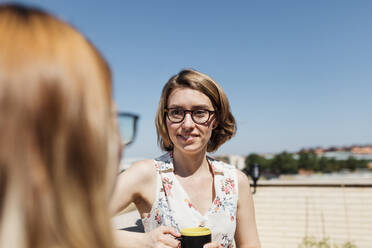 Geschäftsfrau mit Kaffeetasse im Gespräch mit einem Kollegen an einem sonnigen Tag - MRRF01327