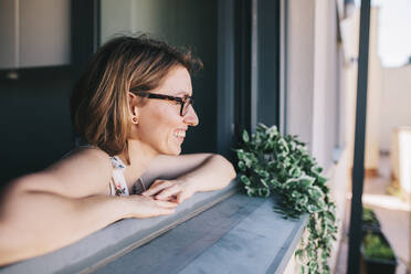 Smiling businesswoman with eyeglasses leaning on window - MRRF01329