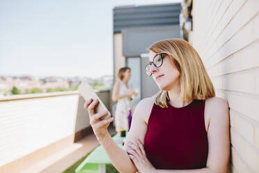 Businesswoman using mobile phone while standing at rooftop - MRRF01341