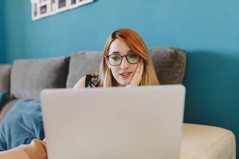 Businesswoman with hand on chin using laptop while working at home - MRRF01354