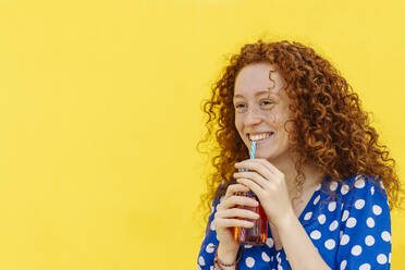 Smiling woman drinking juice in front of yellow wall - JCZF00792