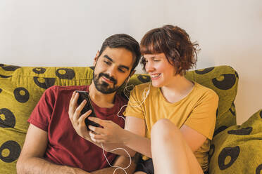 Smiling woman sharing mobile phone with boyfriend on sofa at home - MGRF00387