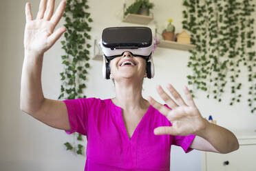 Happy mature woman wearing virtual reality headset at home - JCCMF03580