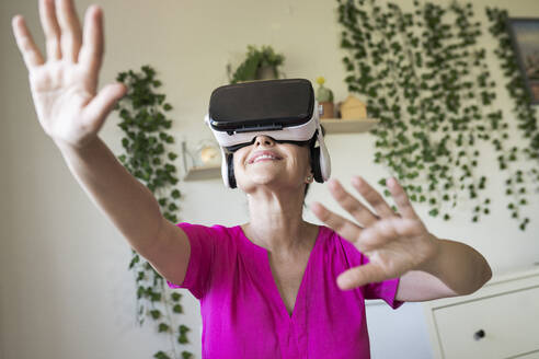 Frau gestikuliert, während sie die virtuelle Realität über ein Headset zu Hause genießt - JCCMF03581