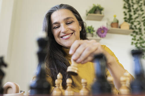 Smiling woman playing chess at home - JCCMF03583