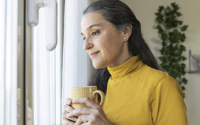 Reife Frau, die nachdenklich ist und einen Kaffeebecher zu Hause hält - JCCMF03585