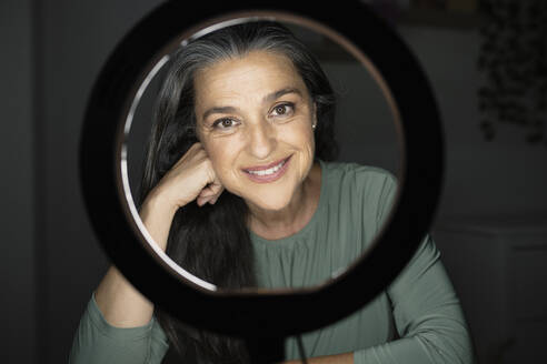 Smiling beautiful woman seen through ring light in darkroom - JCCMF03591