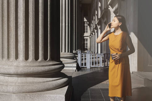 Frau mit Kaffee in der Hand, während sie in der Nähe der Säule der Nationalgalerie in Singapur mit ihrem Smartphone telefoniert - EAF00071
