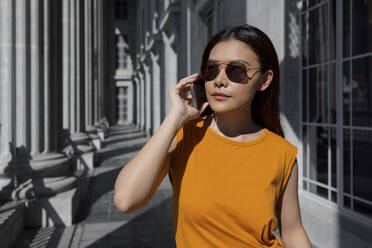Frau mit Sonnenbrille, während sie in der Nationalgalerie Singapur mit einem Smartphone telefoniert, Singapur - EAF00077