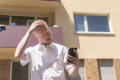 Deutschland, Köln, Albino-Mann im weißen Hemd hält Smartphone - ISF24909