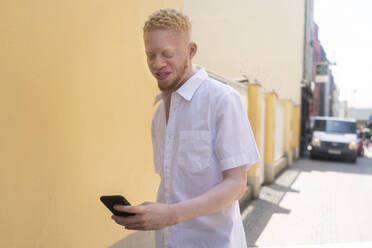 Deutschland, Köln, Albino-Mann im weißen Hemd hält Smartphone - ISF24915