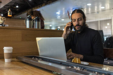 UK, London, Man using laptop and smart phone at airport cafe - ISF24927