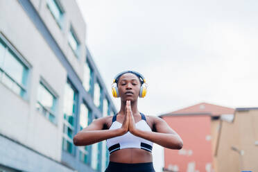 Italy, Milan, Woman with headphones meditating in city - ISF24940