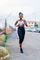 Italy, Milan, Woman with headphones jogging in city - ISF24941