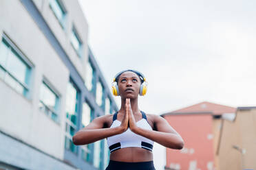 Italy, Milan, Woman with headphones meditating in city - ISF24942