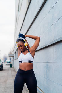 Italy, Milan, Woman in sports clothing and headphones stretching in city - ISF24949