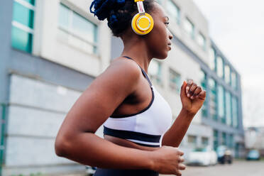 Italy, Milan, Woman with headphones jogging in city - ISF24955