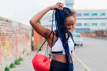 Italy, Milan, Woman in sports clothing doing her long braided hair in city - ISF24958