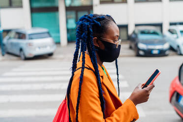 Italy, Milan, Fashionable woman with face mask holding smart phone on street - ISF24967