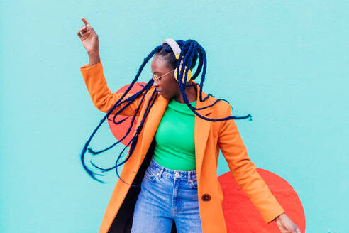 Italy, Milan, Stylish woman with headphones dancing against wall - ISF24970