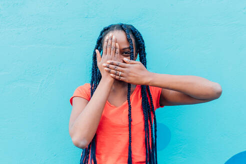 Italy, Milan, Young woman covering mouth and eye in front of blue wall - ISF24985