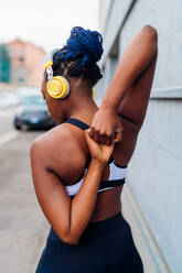 Italy, Milan, Rear view of woman in sports clothing and headphones stretching - ISF25015