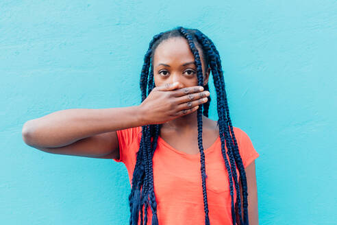 Italien, Mailand, Junge Frau, die den Mund vor einer blauen Wand bedeckt - ISF25023