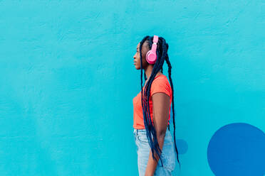 Italien, Mailand, Profil einer jungen Frau mit Kopfhörern vor einer blauen Wand - ISF25037