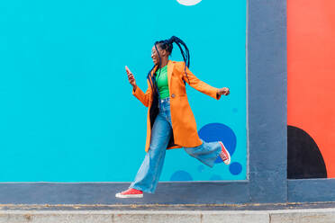 Italy, Milan, Woman with braids jumping against blue wall - ISF25038