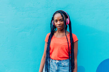 Italy, Milan, Portrait of young woman with headphones in front of blue wall - ISF25042