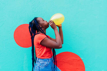 Italy, Milan, Young woman with braids blowing yellow balloon - ISF25057