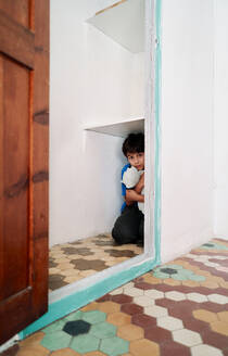 Unglücklicher, verängstigter kleiner Junge mit Spielzeug, der sich im Kleiderschrank versteckt, während er unter häuslicher Gewalt leidet - ADSF28587