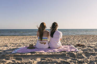 Freundinnen schauen auf das Meer, während sie auf einer Picknickdecke sitzen - JRVF01596