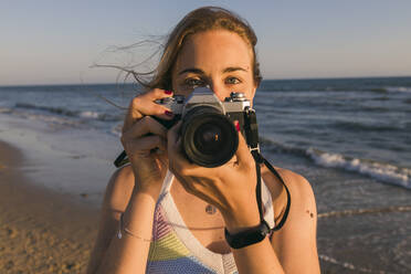 Frau hält Kamera in der Nähe von Meer am Strand - JRVF01605