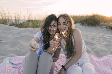 Young female friends burning sparklers at beach - JRVF01609