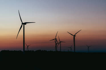 Silhouetten von Windturbinen gegen den stimmungsvollen Himmel in der Abenddämmerung - OCAF00687