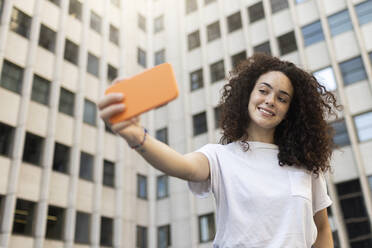 Frau macht Selfie mit Smartphone vor einem Gebäude - MTBF01086