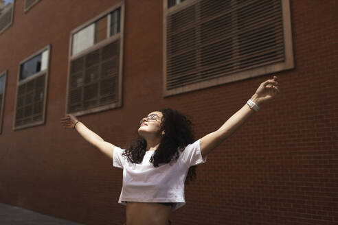 Carefree woman with arms outstretched by building - MTBF01110