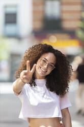 Lächelnde Frau mit Friedenszeichen an einem sonnigen Tag - MTBF01113
