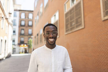 Junger Mann mit Brille lächelt vor einem Gebäude - MTBF01118