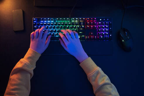 Boy typing on multi colored keyboard at table - VPIF04620