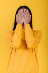 Unerkennbare weibliche Abdeckung Gesicht mit Händen auf hellen gelben Hintergrund in modernen Studio - ADSF28741