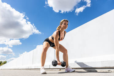 Young woman training with her dumbbell outdoors, arm down, side view - ADSF28765