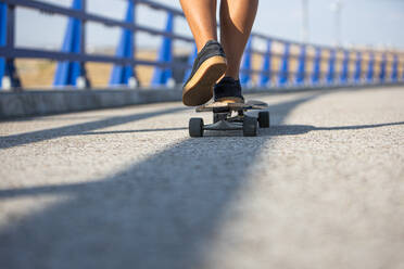 Frauen Füße Skaten Longboard durch eine leere Brücke bei Sonnenuntergang, Rückansicht - ADSF28774