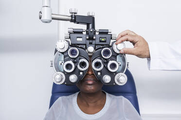 Optometrist, der die optometrische Ausrüstung während der Untersuchung der Sehkraft einer schwarzen Frau einstellt - ADSF28782