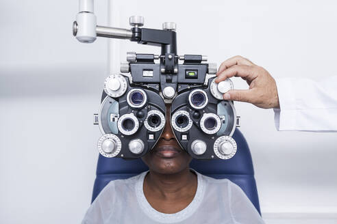 Optometrist, der die optometrische Ausrüstung während der Untersuchung der Sehkraft einer schwarzen Frau einstellt - ADSF28782