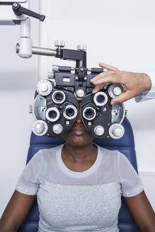 Optometrist, der die optometrische Ausrüstung während der Untersuchung der Sehkraft einer schwarzen Frau einstellt - ADSF28783